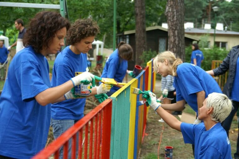 Women in blue T-shirts paint the fence in different colors